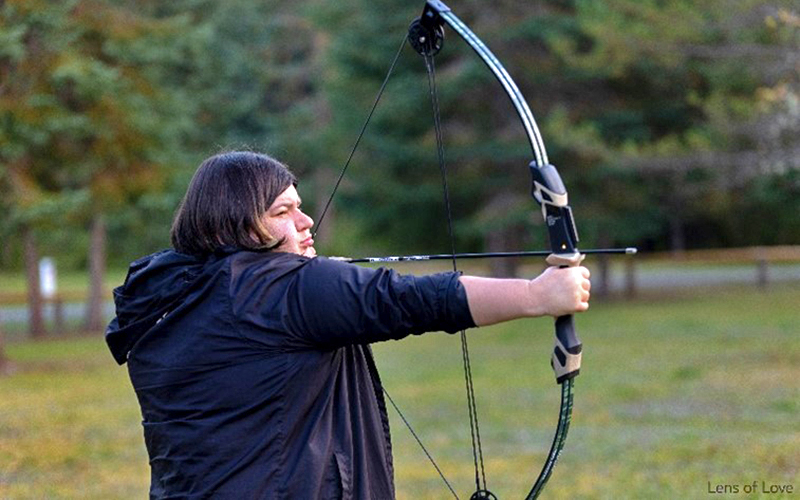 A women holds a bow and arrow and prepares to shoot the arrow.