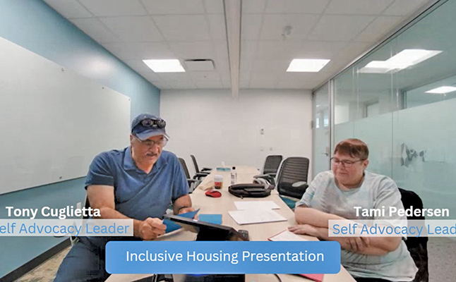 A man and a woman sit on opposite sides of a table and give a presentation together.
